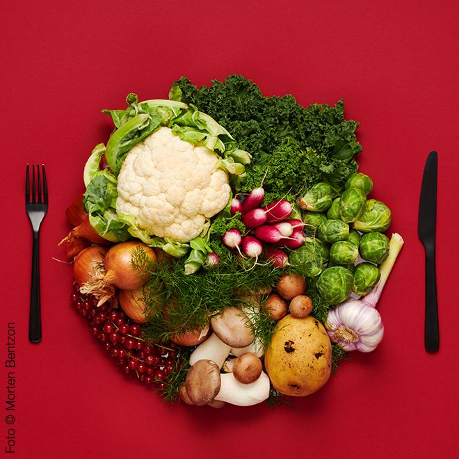 Dekoratives Bild mit einem großen Gemüseteller und Essbesteck vor rotem Hintergrund